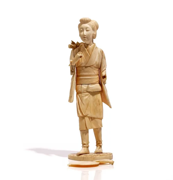 A Japanese sectional ivory okimono of a young woman, Meiji period, carved standing carrying vegetables across her shoulders and with a fan in her left