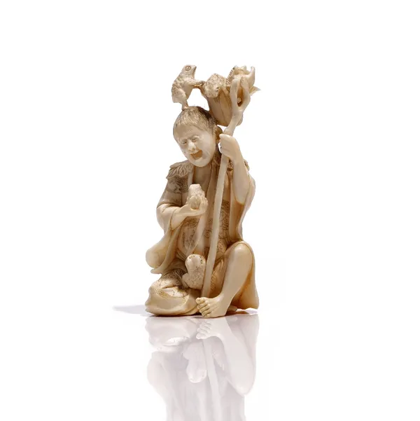 A Japanese ivory okimono, Meiji period, carved as a man seated with toads, holding a staff suspending a lotus flower basket,  signed, 11cm. high.