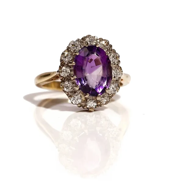 A gold, amethyst and diamond set oval cluster ring, claw set with the oval cut amethyst at the centre in a surround of twelve circular cut diamonds, r