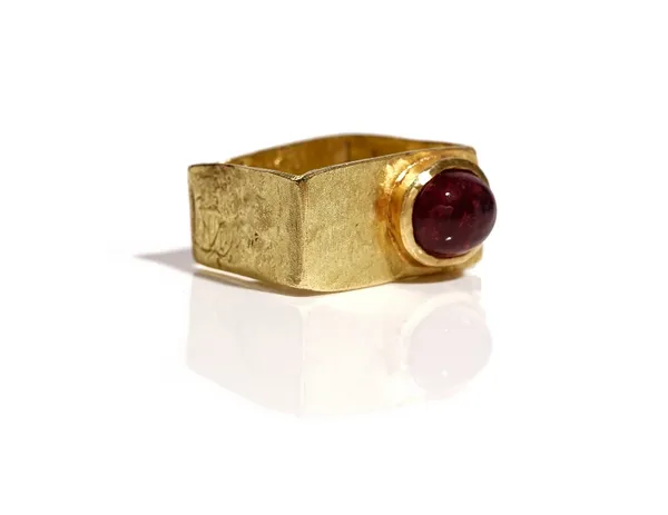 An 18ct gold ring of rectangular form, mounted with an oval cabochon pink tourmaline, otherwise having a textured finish, maker's mark DEJA, gross wei