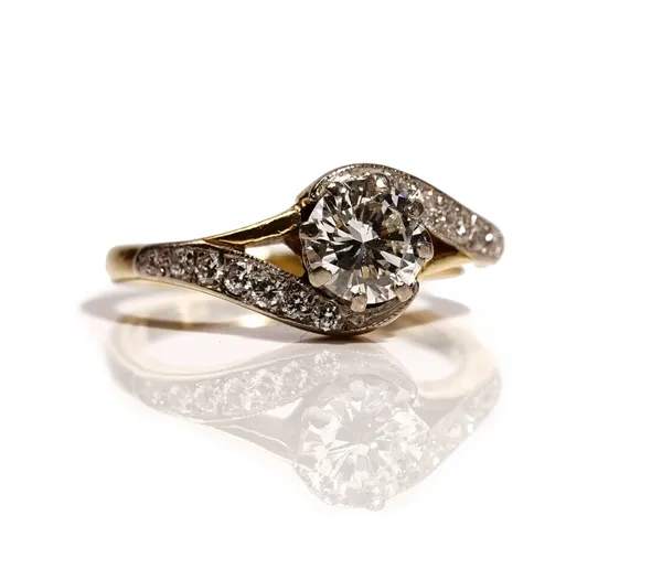 An 18ct gold single stone diamond ring of cross over design, the brilliant-cut diamond approximately 1.00 ct,  eight claw set  in a wave-scroll mount,