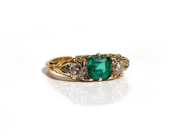 A gold, emerald and diamond ring, mounted with the square step cut emerald to the centre, between the two principal cushion shaped diamonds and with s