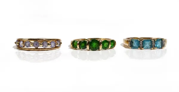 A 9ct gold and diopside five stone ring, a 9ct gold and mauve gem set seven stone ring and a 9ct gold ring, mounted with three square cut blue stones