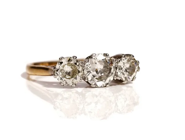 A gold and platinum, diamond set three stone ring, claw set with a row of cushion shaped diamonds and with the principle diamond mounted to the centre