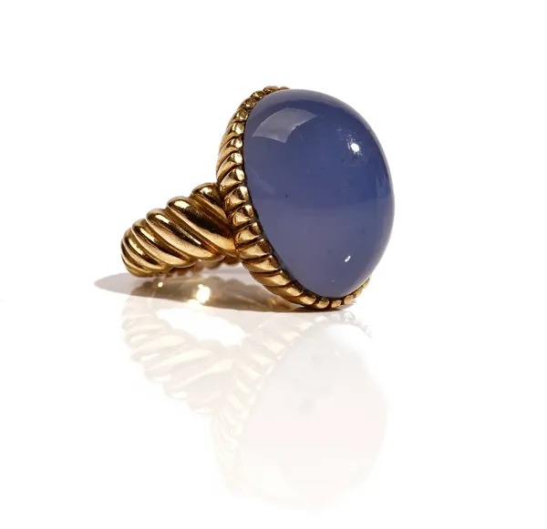 A gold ring, mounted with an oval cabochon blue stained chalcedony, the setting with ridged decoration, the shank with slanting ridged decoration, det