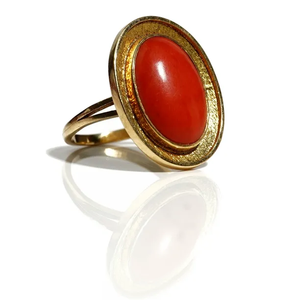 A gold mounted oval coral ring, the oval coral mounted within a textured border, ring size O and a half, unmarked, gross weight 8 gms.