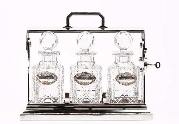 A silver plated tantalus, 20th century, with three cut glass decanters having silver labels, each detailed 'PORT', 'GIN' and 'BRANDY', hallmarked for