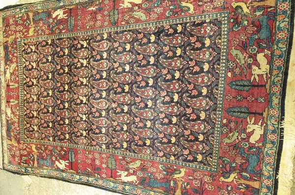 A Tehran rug, Persian, the dark indigo field with rows of botehs; a burgundy border of trees, birds, hares and hunting dogs, 214cm x 134cm.