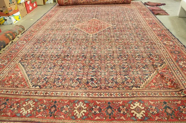 A Hamadan carpet, Persian, the dark indigo field with a bold madder diamond, and spandrels, with an allover herate design; a madder flowerhead, palmet