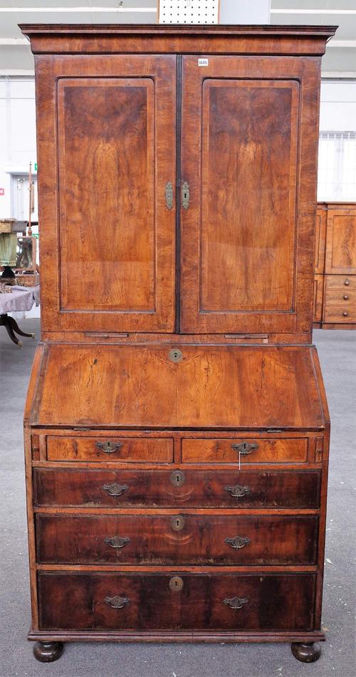 A George II walnut cross and featherbanded bureau cabinet, the upper part with above adjustable shelves enclosed by a pair of doors, two candle slides