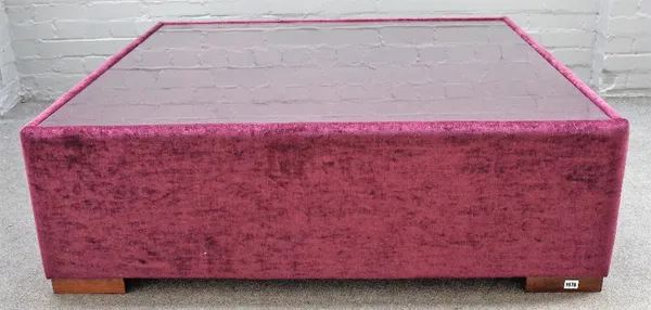 A large square plum coloured upholstered coffee table, with inset glass top on block supports, 130cm wide x 42cm high.