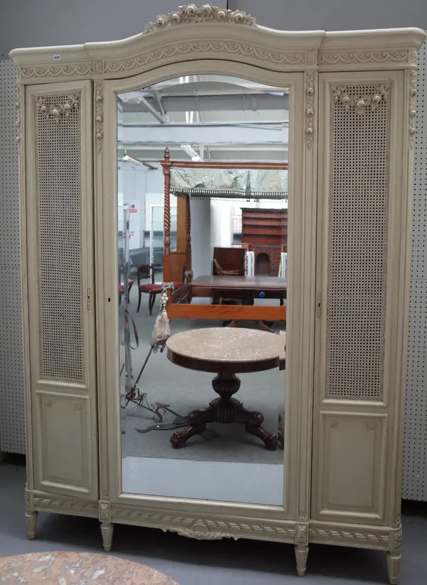 A Louis XVI style white painted wardrobe, 21st century, with foliate carved ornament, the arched cornice above bergere panels flanking a centre mirror