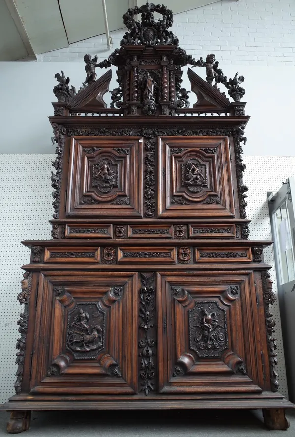 A large early 18th century Italian walnut double height cabinet, with extensive relief carved decoration, the architectural cornice over two pairs of