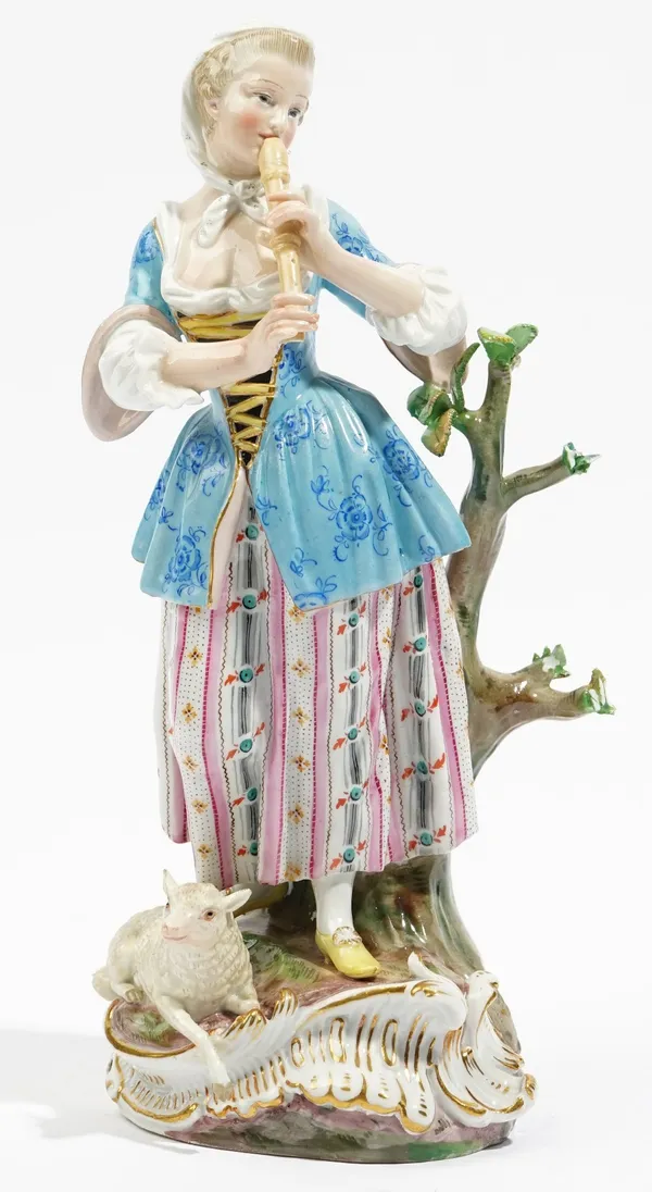 A Meissen figure of a shepherdess, late 19th century, standing against a tree stump playing the recorder, a lamb recumbent at her feet, blue painted c