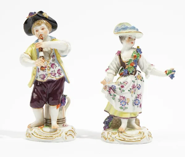 A pair of Meissen figures of vintners, 20th century, a boy playing a recorder, his companion holding grapes, each with a jug or basket of grapes at th