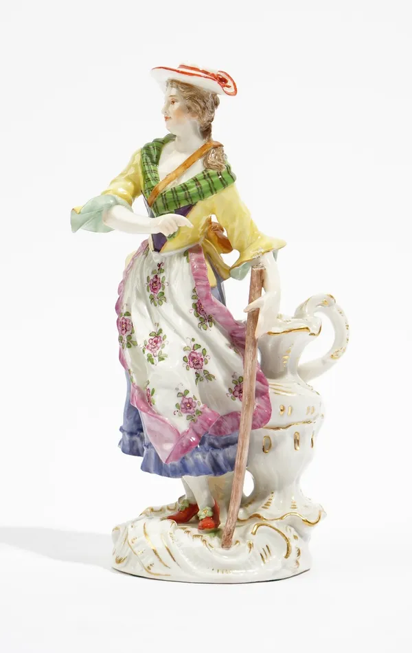 A Meissen figure of a shepherdess, early 20th century, modelled standing beside a large ewer and holding a staff in her left hand, blue crossed swords