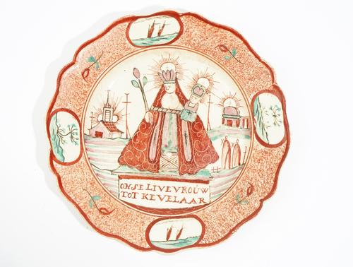 A small Dutch decorated Leeds creamware plate, circa 1775-85, painted with the Virgin Mary and Jesus flanked by chapels above the inscription, `Onse L