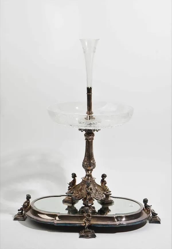 A silver plated metal mounted glass table centrepiece, the base with three seated putto, with foliate divisions at intervals, the stems supporting a f