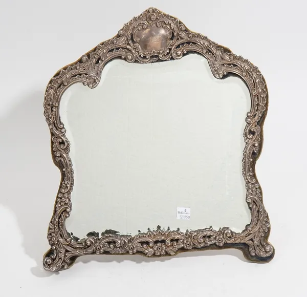 A silver mounted strut backed mirror, the mount embossed and pierced with floral, foliate and scrolling decoration, the fitted glass having bevelled e