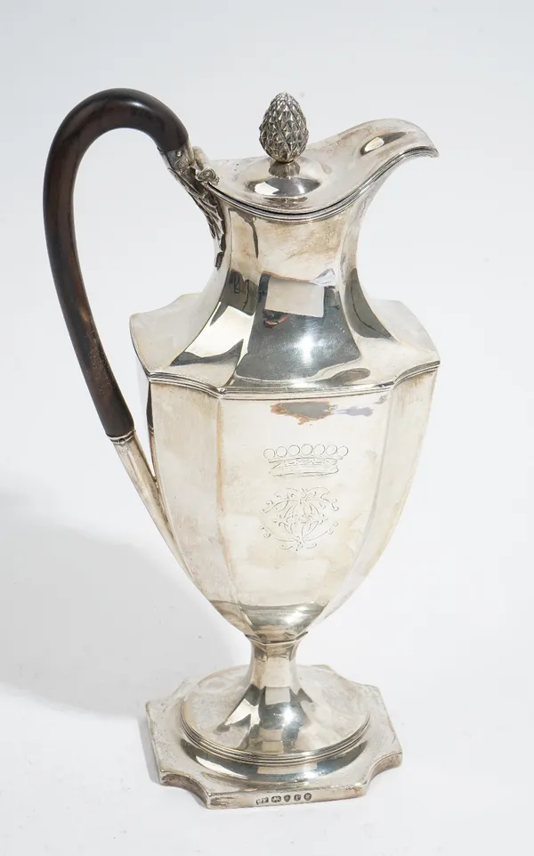 A George III silver hot water jug, of panelled Adam form, engraved with a coronet above a monogram to each side, the hinged lid with a pine cone finia