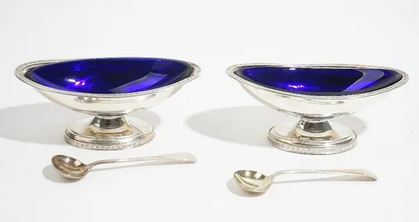 A pair of silver salts, each of boat shaped form, having flowerhead motifs to the rims, Birmingham 1908, with two blue glass liners and a pair of Old