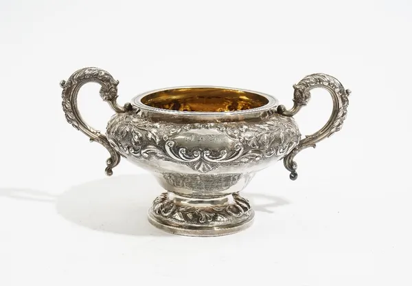 A Victorian silver twin handled sugar bowl, of squat circular form, with foliate decorated scrolling handles, otherwise decorated with foliate bands,