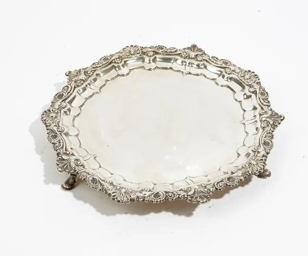 A George IV silver shaped circular salver, the shaped border with cast shell and scrolled decoration in the Chippendale style, raised on three pad fee