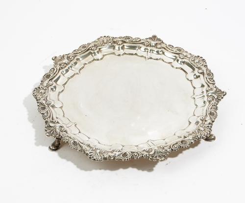 A George IV silver shaped circular salver, the shaped border with cast shell and scrolled decoration in the Chippendale style, raised on three pad fee