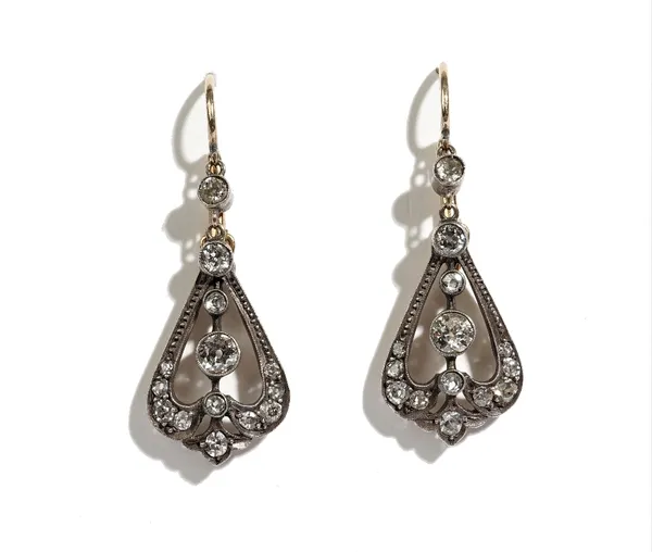 A pair of gold backed and silver set diamond pendant earrings, each in a scroll pierced tapered design, mounted with cushion shaped diamonds and with