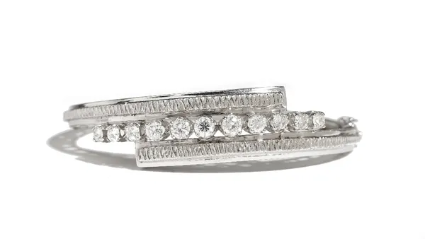 A diamond set oval hinged bangle, claw set with a row of eleven circular cut diamonds graduating in size to the centre stone, between ridged sides in