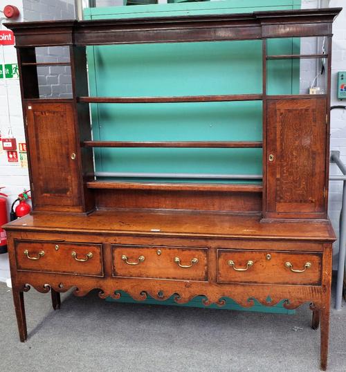 An 18th century mahogany banded oak dresser, the open three tier plate rack, with pair of cupboards, the base with three drawers over shaped frieze,...