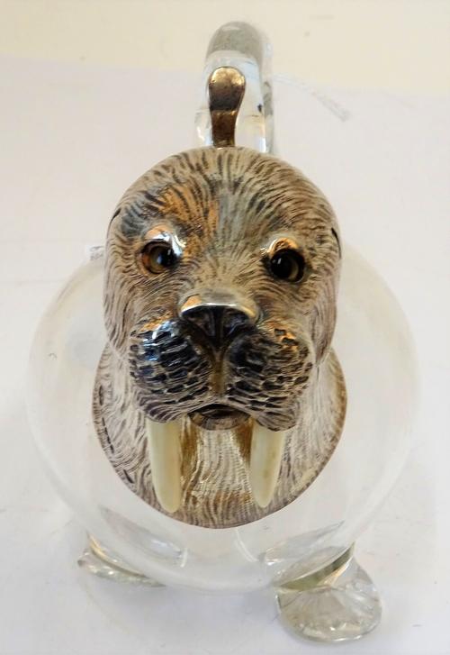 A Victorian silver mounted moulded colourless glass claret jug, designed as a walrus, having a hinged lid and glass eyes, London 1881, maker...