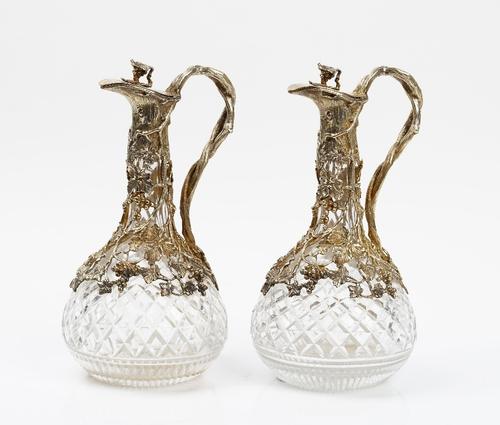 A pair of base metal mounted faceted glass claret jugs, late 20th century, retailed by Garrard & Co, the mounts cast and pierced with fruiting vines,...