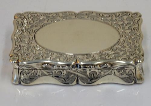 A Victorian silver shaped rectangular hinge lidded snuff box, the exterior with scroll engraved decoration, the lid with a vacant oval cartouche,...