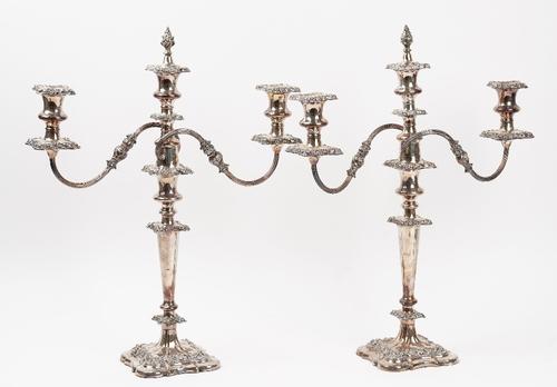 A pair of plated on copper three light table candelabra, with scrolling arms, central detachable flame finials, each raised on a shaped square base,...