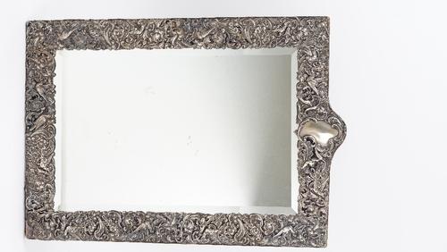 A late Victorian silver mounted shaped rectangular large strut backed mirror, the mount embossed and pierced with cherubs, birds and floral scrolls,...