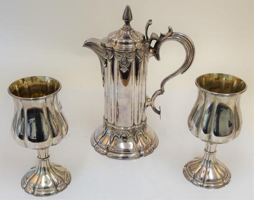 A plated wine flagon, with a matching pair of goblets, the flagon of Gothic design, with a scrolled handle and pointed finial to the hinged lid,...