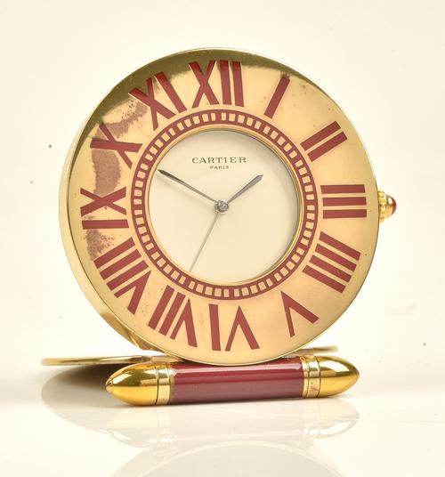 A Cartier Paris quartz folding travelling clock, of gilt metal circular form, the signed dial with outer red enamelled Roman numerals, detailed to...