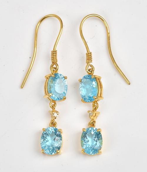 A pair of 18ct gold, diamond and blue topaz pendant earrings, each claw set with two oval cut blue topaz and with a small circular cut diamond at the...