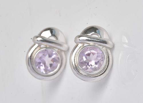 COLLECTED 06.08.2021. A pair of white gold and amethyst single stone earstuds, each in a hoop shaped and bar design, collet set with a circular cut amethyst, the backs...