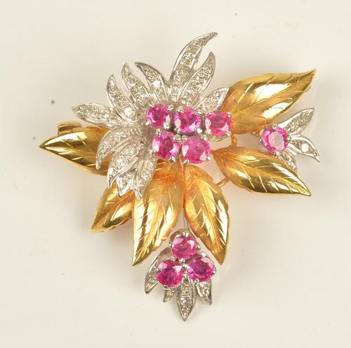 An 18ct two colour gold, ruby and diamond brooch, designed as a floral and foliate spray, mounted with circular cut rubies and with smaller circular...