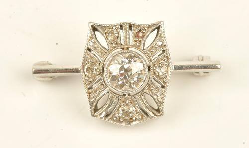 A diamond brooch in a pierced curved panel shaped design, mounted with the principle cushion shaped diamond to the centre and otherwise further set...