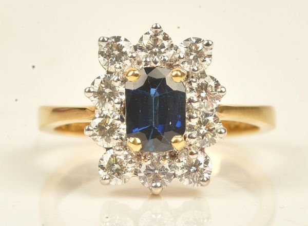 A gold, sapphire and diamond eleven stone cluster ring, claw set with the cushion shaped sapphire at the centre, in a surround of ten circular cut...