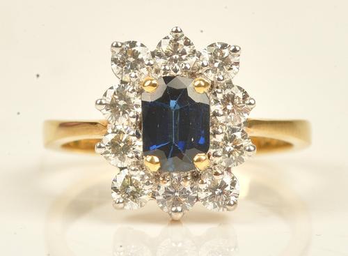 A gold, sapphire and diamond eleven stone cluster ring, claw set with the cushion shaped sapphire at the centre, in a surround of ten circular cut...