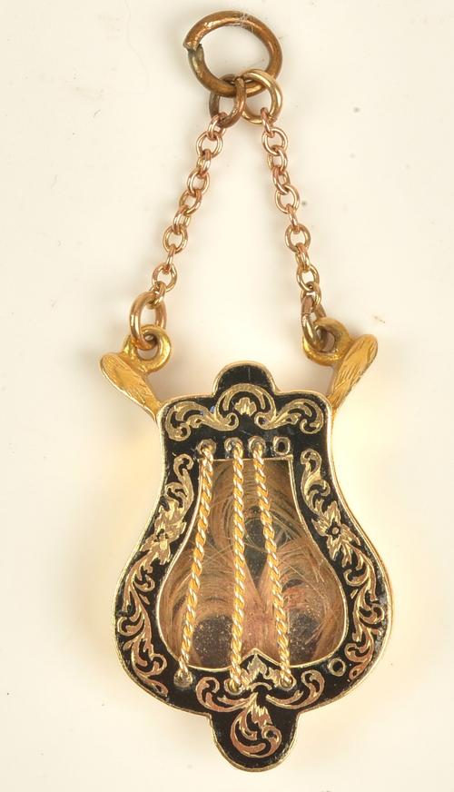 A Victorian gold and black enamelled pendant locket, designed as a lyre, the hinged front opening to reveal a glazed feathered hair locket, the back...