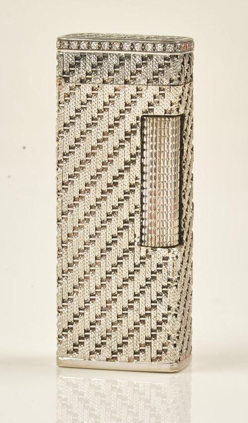 A white gold cased and diamond set rectangular gas lighter, the exterior decorated with textured stripes and mounted with a border of circular cut...