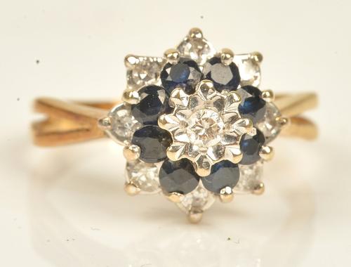 A gold, diamond and sapphire cluster ring, mounted with a circular cut diamond to the centre, in a surround of eight circular cut sapphires and with...