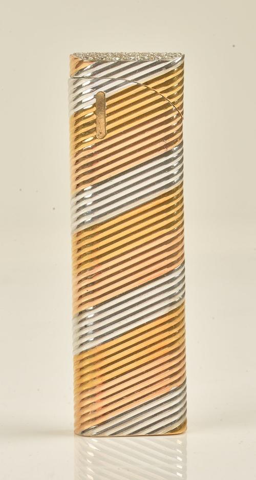 A Colibri two colour gold and diamond set, curved rectangular cased gas lighter, the sliding sprung top pave set with circular cut diamonds,...