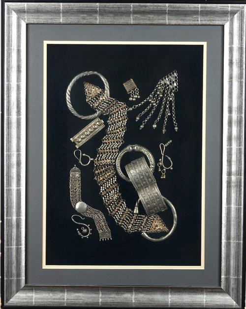 A collection of tribal silver coloured metal jewellery, possibly North African Beduin, including bangles, ear pendants and chains, displayed in a...