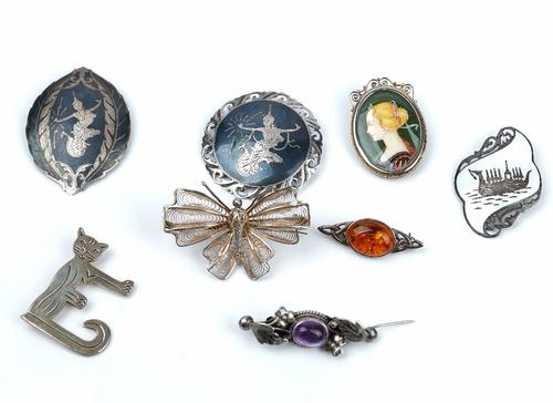 A group of mostly silver jewellery, comprising; eight brooches, a reconstituted amber pendant with a neckchain, seven further pendants and charms, an...